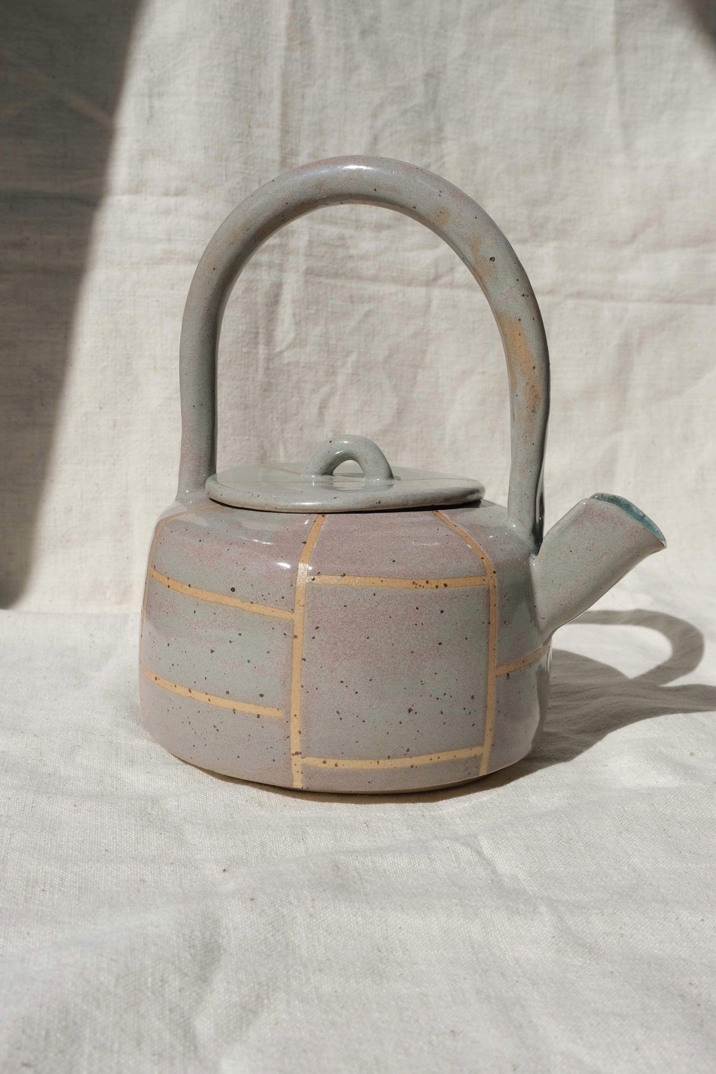 Side view of a handmade ceramic teapot in toasted sage and pink with grid lines