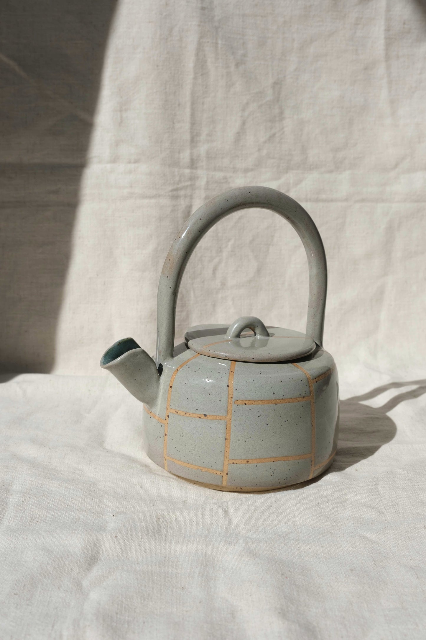 Side view of a handmade ceramic teapot in toasted sage with grid lines