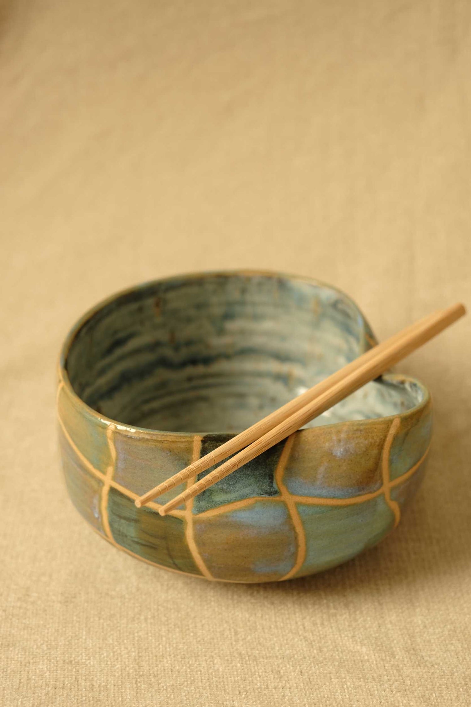 Ceramic bowl with a textured surface and wooden chopsticks on a beige background